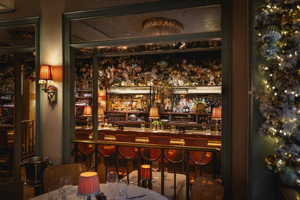 a view of the bar area at daphne's from the outside in, where baubles fill the ceiling amidst rich brass and gold and velvet furnishings