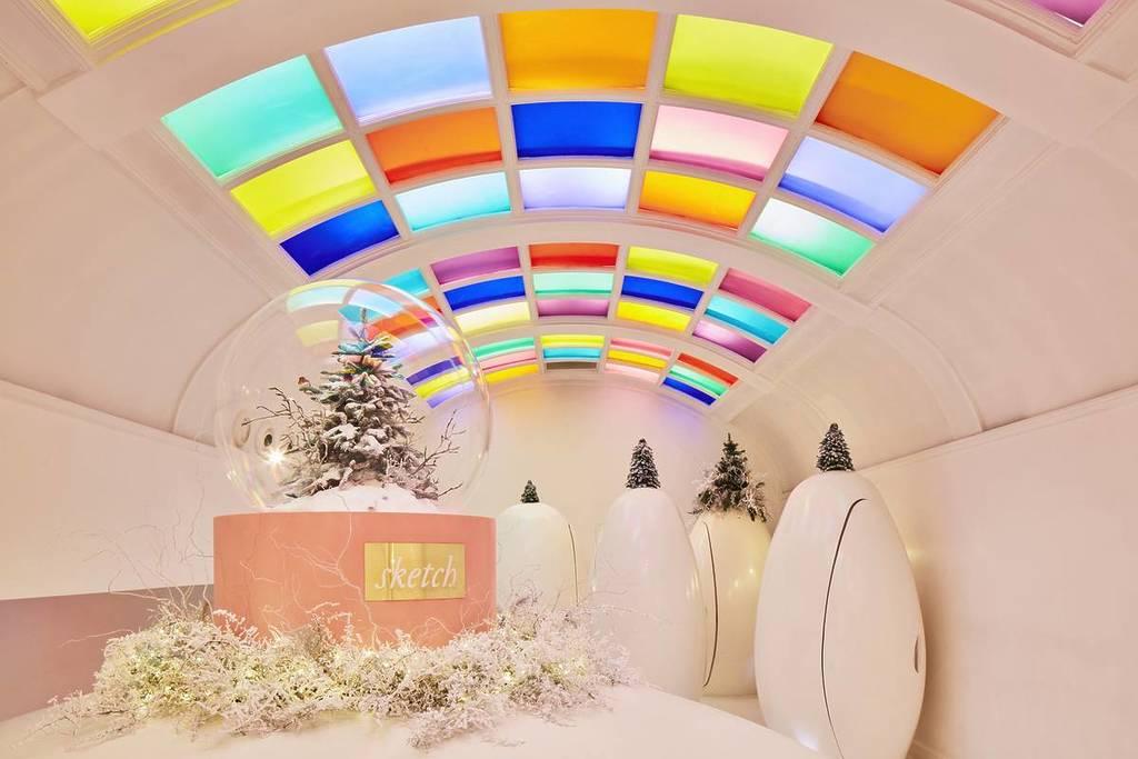 tiny christmas trees perched on top of pods, and a massive snowglobe containing a christmas tree, in sketch's east bar and pods room - with a multi-coloured kaleidoscope of lights and tiles illuminating the room from above