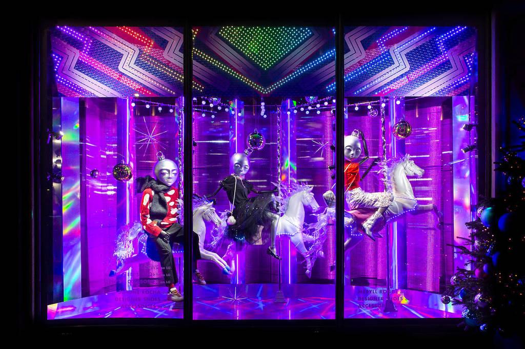 bauble-headed figures atop carousel horses in front of a purple LED light display